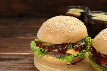 Board with delicious cheeseburgers on wooden table, closeup. Space for text