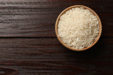 Raw basmati rice in bowl on wooden table, top view. Space for text