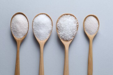 Organic white salt in spoons on light grey background, flat lay