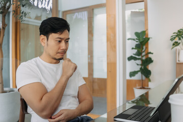 Asian man sitting and using working on computer at cafe, thoughtless, have no idea, freelance concept.