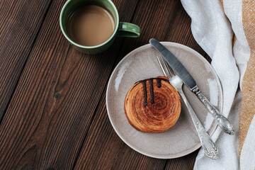 a round New York croissant in a plate, next to a blue vase with snowdrops and a striped towel with cutlery on a dark wooden background