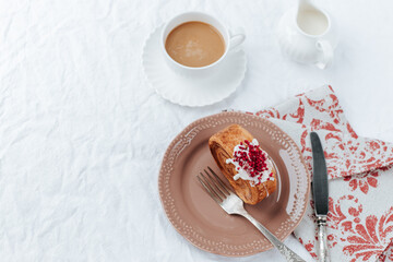 Obraz na płótnie Canvas There is a round croissant on a beige plate.Next to it are a napkin with red patterns and vintage cutlery,a cup of coffee, a milk jug .White backgrounds, shots from above