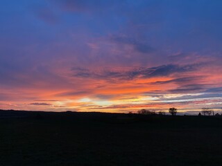 Coucher de soleil avec ciel orange et rouge, nuages colorés, et horizon illuminé, offrant un paysage panoramique de crépuscule et de lumière, avec des silhouettes et des couleurs vives en soirée.