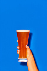 Woman holding long glass with fresh beer isolated on blue background. Chill drops falling down....