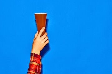 Male hand holding long glass with fresh beer isolated on blue background. Traditional taste. Party....