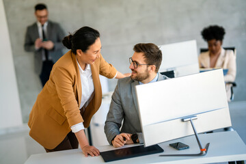 Senior business manager talking with experienced colleague while using computer in office.
