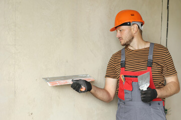 Rear view of handyman worker in overalls and protective helmet plastering concrete wall with putty...