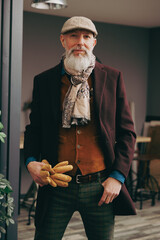 Portrait d'un homme original gentleman quinquagénaire senior hispter élégant et stylé avec un manteau un béret et un gilet dans un atelier créatif