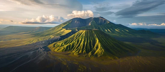 Fotobehang Aerial view of a mountain range with a volcano surrounded by clouds in the sky, creating a dramatic natural landscape with lush green plants and water bodies © TheWaterMeloonProjec
