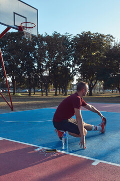 Man exercising and stretching on a public basket court in an urb