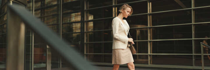 Businesswoman with blond hair wearing beige suit leaving business center, Panorama
