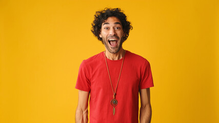 Surprised attractive man with curly hair, dressed in red T-shirt,  covers his mouth with his palms...