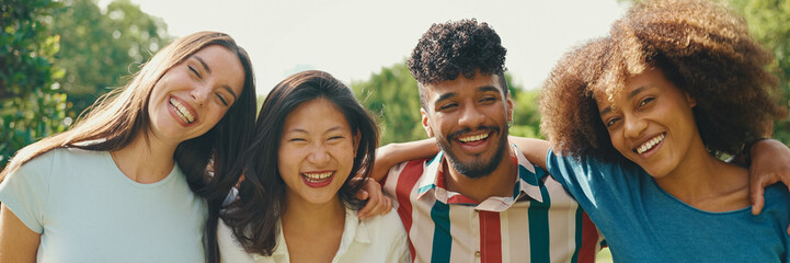 Happy multiethnic young people walk embracing on summer day outdoors. Group of friends are talking and laughing merrily while walking along path in city park, Panorama