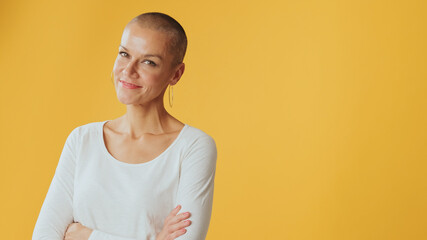 Young hairless woman crossing her arms and looking at camera with smile, advertising space,...