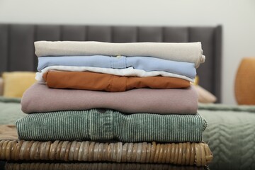 Sorting and organizing. Stack of different folded clothes on wicker table indoors, closeup