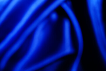 The surface is wavy, silk satin texture. Draped fabric on a blue background, luxurious and beautiful, with space for design, close-up, blur or blur.