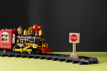 Naklejka premium Road Stop sign as barrier blocking way for toy train on yellow surface, closeup. Development through obstacles overcoming