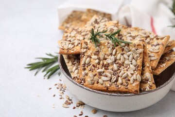 Cereal crackers with flax, sunflower, sesame seeds and rosemary in bowl on light table, closeup. Space for text