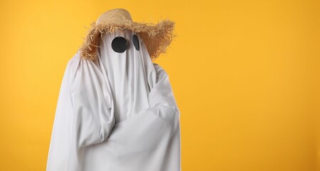 Person in ghost costume and straw hat on yellow background, space for text