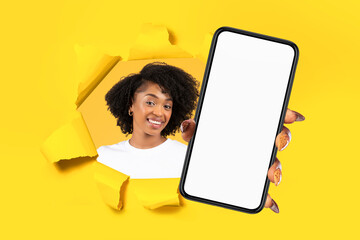 Obraz premium Cheerful young african american woman showing smartphone with empty screen through hole in paper