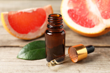 Grapefruit essential oil in bottle, pipette, leaf and fruit on wooden table, closeup