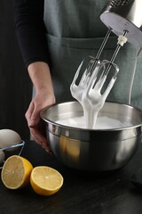 Woman making whipped cream with hand mixer at black table, closeup