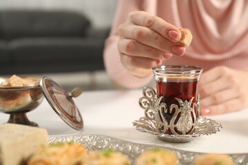Woman adding sugar to delicious Turkish tea at white table, closeup