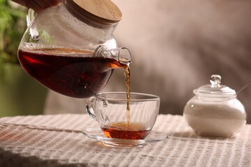 Woman pouring aromatic tea into cup at table, closeup