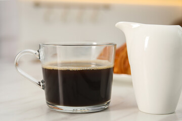 Aromatic coffee in glass cup and pitcher on white marble table