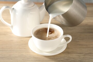 Pouring milk in tea at wooden table, closeup