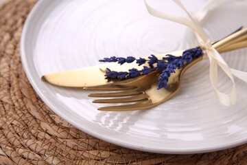 Cutlery, plate and preserved lavender flowers on wicker place mat, closeup