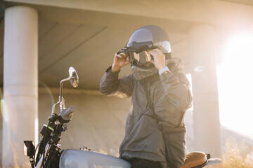 A biker puts on a helmet while sitting on a motorcycle..A man rides a motorcycle at sunset.