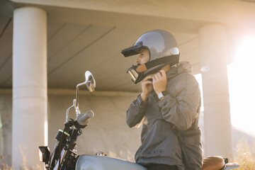 A biker puts on a helmet while sitting on a motorcycle..A man rides a motorcycle at sunset.