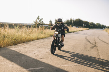 A man with a vintage motorcycle on the highway at sunset. A man drives a cafe racer. Biker lifestyle concept