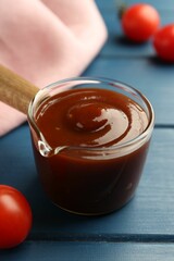 Tasty barbeque sauce and tomato on blue wooden table, closeup