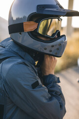 A motorcycle rider fastens his helmet while sitting on a motorcycle on the road against the sunset.