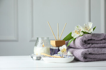 Spa composition. Towels, burning candles, reed air freshener, sea salt and beautiful flowers on white wooden table, space for text