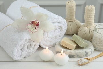 Fototapeta na wymiar Beautiful spa composition. Towels, herbal bags, soap bars and burning candles on white wooden table