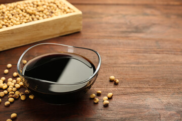 Soy sauce in bowl and soybeans on wooden table. Space for text