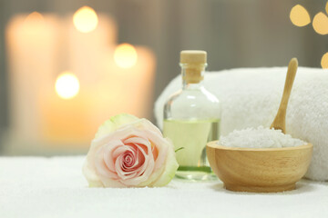 Beautiful spa composition with essential oil, sea salt and rose on white towel against blurred background. Space for text