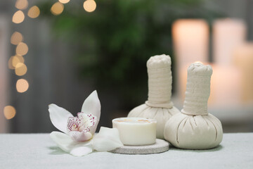 Spa composition. Herbal massage bags, soap bar and orchid flower on white towel against blurred lights, space for text