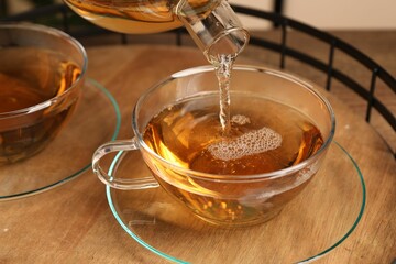 Pouring tasty tea into glass cup at wooden table, closeup