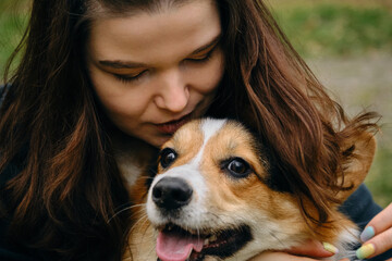 A pretty young Caucasian woman hugs her dog while walking in the park. Portrait of the owner with a pet in close-up. Welsh corgi pembroke tricolor.