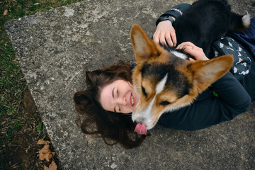 Young woman lies on a concrete slab in the park and hugs her dog. Welsh corgi pembroke and female...