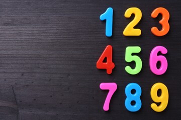 Colorful numbers on dark wooden school desk, flat lay. Space for text