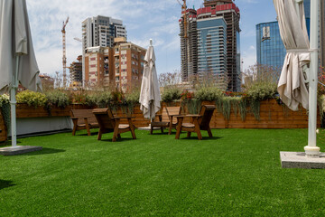 Urban rooftop garden with wooden furniture, artificial grass, and cityscape backdrop in Ramat Gan,...