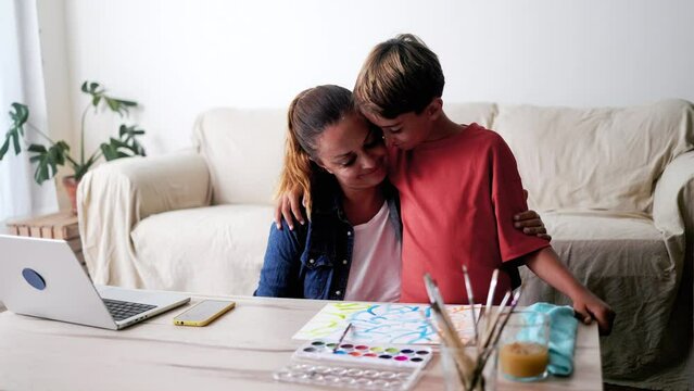 Latin American business mother hugging child son while using computer laptop at home. Family lifes tyle