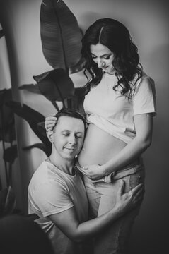 Cropped image of husband listens baby in belly pregnant wife. Pregnant woman and loving handsome man hugging tummy at home. Parenthood concept. Couple waiting baby. Nine months. Black and white photo