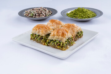 Close up view of traditional Turkish cuisine dessert, pistachio baklava on a white plate. Ground and raw pistachios in copper plates isolated on white background.