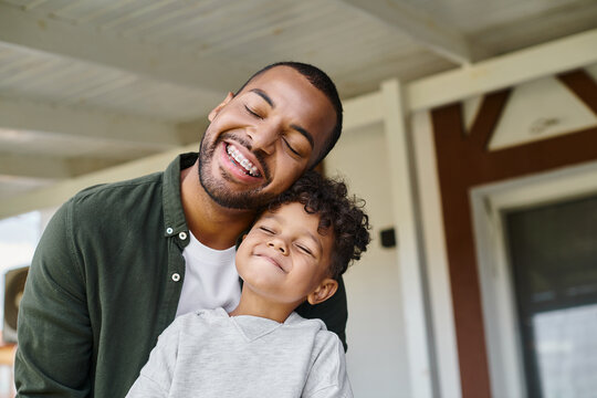 joyful african american boy and cheerful father smiling with closed eyes while having good time